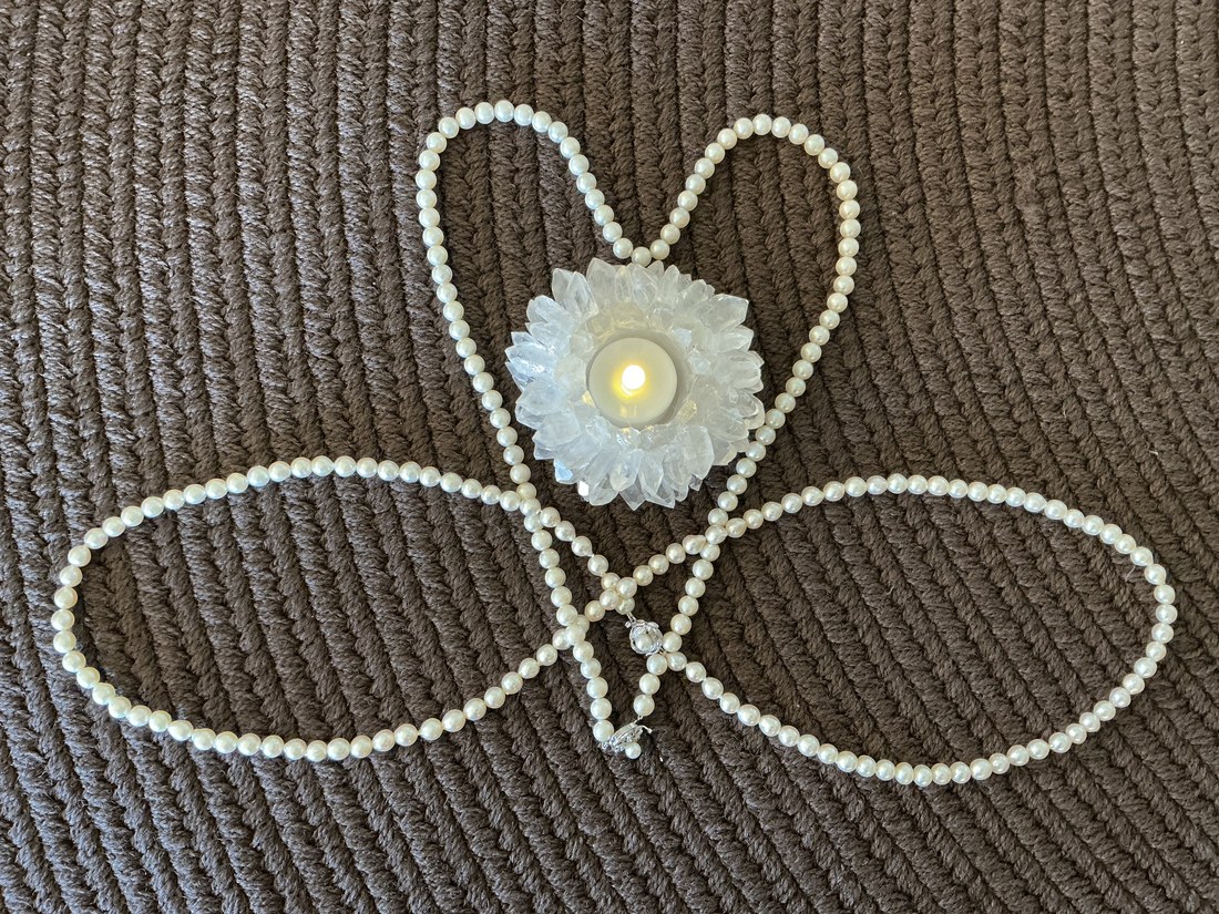 An infinity sign of pearls interwoven with a heart, holding a lit candle in a crystal lotus